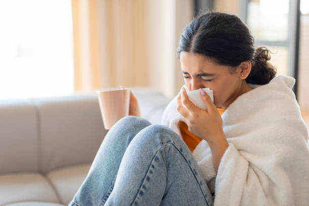 istock Sick young indian woman wrapped in blanket, blowing her nose with tissue 2000663547