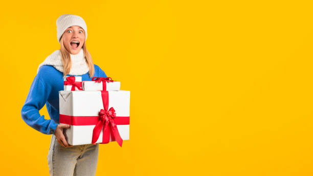 istock Happy lady with stack of X-mas boxes, standing over yellow studio background, panorama, free space 2000665765