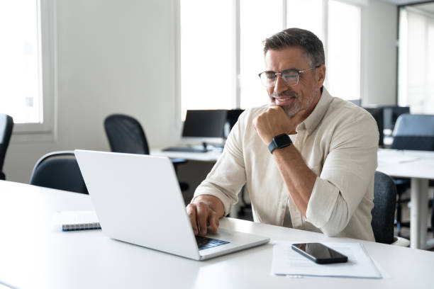 istock Businessman doing online data market analysis, thinking planning tech strategy at laptop. Happy smiling mature Indian or Latin business man ceo trader using computer, typing, working in modern office. 2000672717