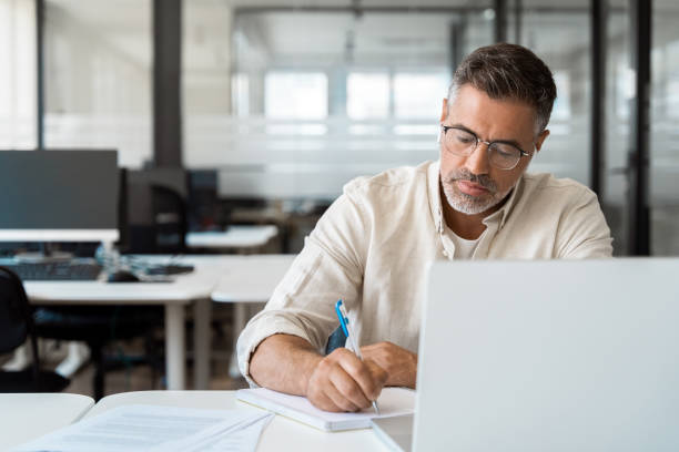 istock Focused middle-age Hispanic man using laptop computer for business studying, watch online virtual webinar training meeting, video call, make notes. Mature Latin businessman work in office, copy space. 2000672722