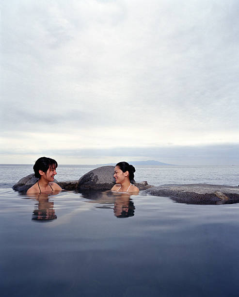 Two young women soaking in hot spring, sea in background Sagami Bay, Izu-Hokkawa, Izu Peninsula, Japan sagami bay photos stock pictures, royalty-free photos & images