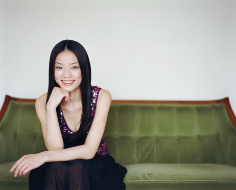 Young woman sitting on sofa, resting chin on hand, smiling