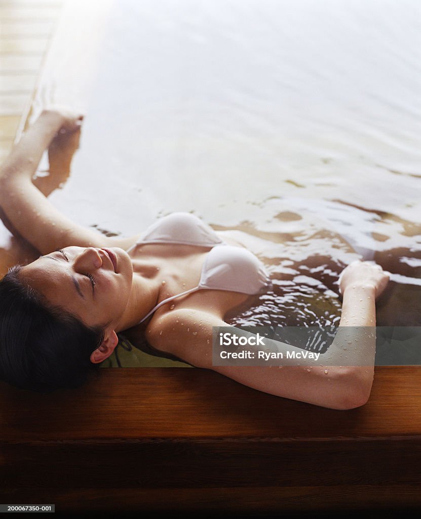 Young woman soaking in hot spring bath, eyes closed, elevated view Japan Hot Tub Stock Photo