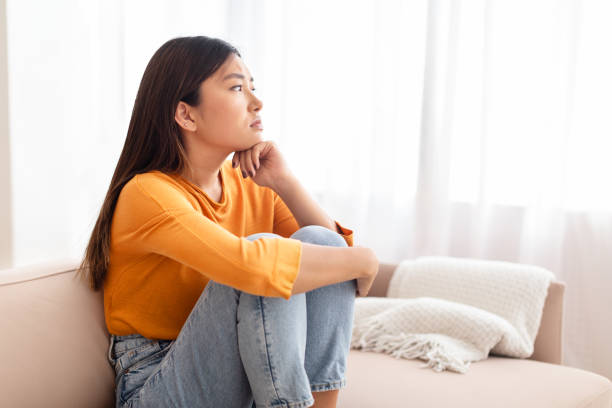istock Frustrated young asian woman sitting on sofa at home 2000747591