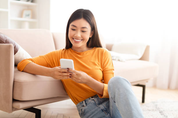istock Cute young asian woman sitting on floor, using phone 2000747593