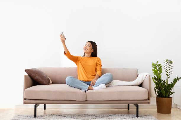 istock Relaxed millennial korean woman sitting on couch, turning on AC 2000748148