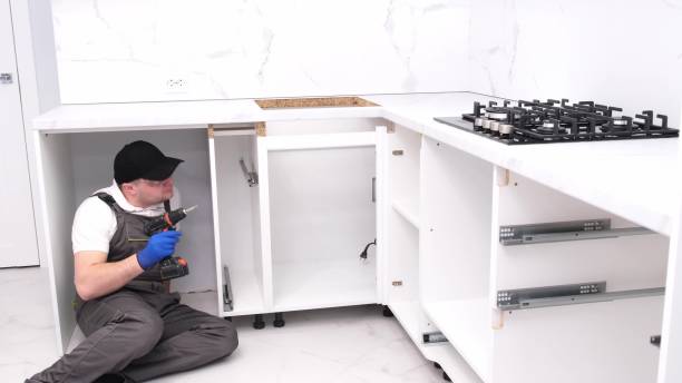 Male repairman assembles furniture using an electronic screwdriver. Installation of furniture stock photo