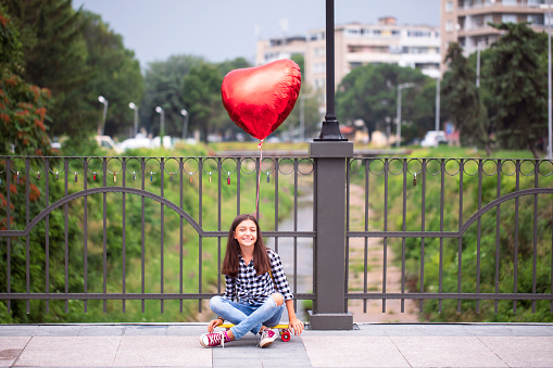 Cool teenage girl with skateboard and heart shape balloon.