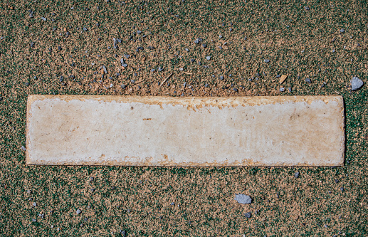 Looking down at a worn out pitcher’s mound rubber on a dirt covered artificial turf mound used for warmups in a small town baseball field.