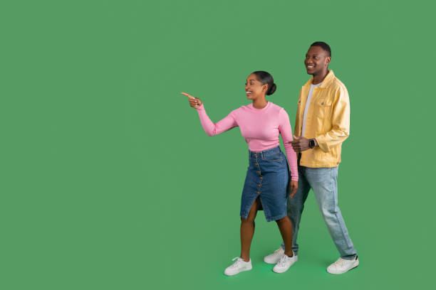 istock Cheerful black couple pointing at copy space, green background 2000862456