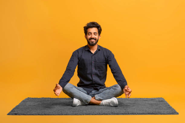 jovem indiano relaxado em roupas casuais meditando sozinho, sentado de pernas cruzadas em carpe - men yoga meditating cross legged - fotografias e filmes do acervo