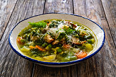 Pistou soup Nice - broth with basil pesto, bread, grated cheese and vegetables on wooden table in white bowl