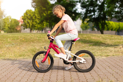 Pretty schoolgirl riding a bike alone in park, children and sports, physical activity outdoors, cycling, healthy lifestyle, recreation and leisure