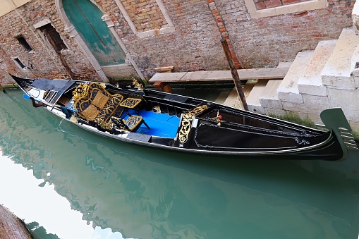 Venice, July 2016. The gondola, a sleek black silhouette against the sun-drenched water, glides effortlessly through the narrow passage. Its ornately carved prow, devoid of the usual tourist trinkets, reflects the understated elegance of the setting. Instead of plush velvet cushions, worn wooden benches offer a rustic charm, inviting you to imagine the countless stories they've witnessed.