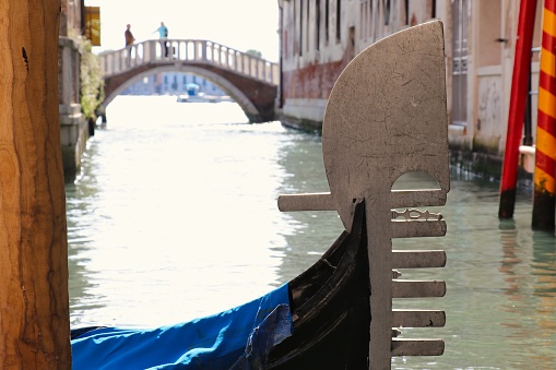 Venice, July 2016. a glimpse into a quiet side canal, far from the tourist crowds. Sunlight filters through the narrow gap between weathered buildings, casting dappled shadows on the water. A single gondola, painted a unique turquoise, is moored at a stone bridge, its plush velvet seats inviting exploration. Ivy creeps up the walls, adding a touch of mystery to the scene.