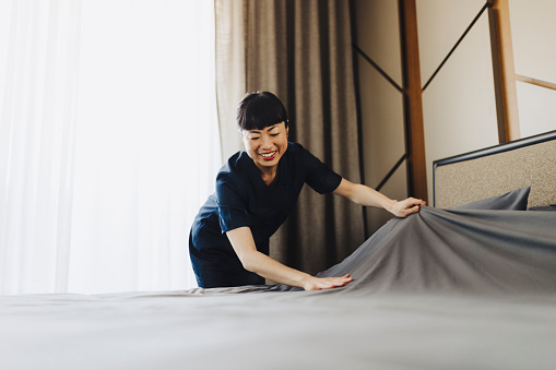 Chambermaid changing bed linen on the bed in a hotel room