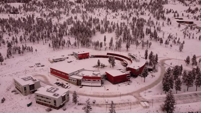 A circular building sits next to a dense forest and snow-covered mountains in the city of Merritt, British Columbia.