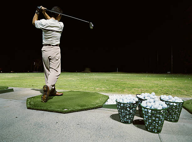 Man practicing golf on  driving range at night, rear view  night golf stock pictures, royalty-free photos & images