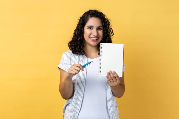istock Joyful smiling woman standing holding paper notebook and showing empty paper, copy space. 2001251720