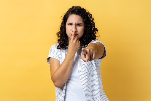 I don't believe, you are liar. Dissatisfied woman with dark wavy hair in business suit touching nose showing lie gesture, suspecting cheating. Indoor studio shot isolated on yellow background.