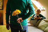 Senior man hiding a bouquet of yellow daffodils behind back to surprise his wife