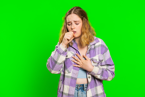 Unhealthy young caucasian woman coughing with seasonal flu symptoms covering mouth with hand, feeling sick, allergy, fever or viral infection. Unwell ill girl isolated on green chroma key background