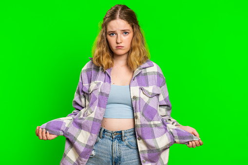 Unemployed poor young caucasian woman showing empty pockets, no money, lost cash, debt problems, poverty, financial crisis, jobless and bankruptcy. Redhead girl isolated on green chroma key background