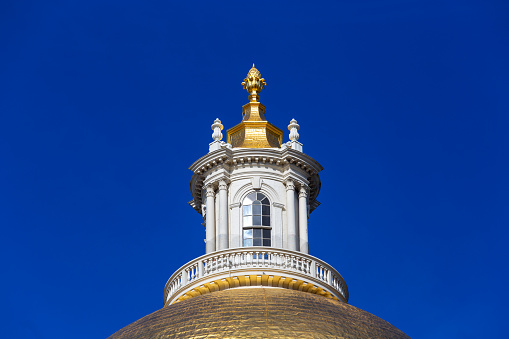 Boston, Massachusetts, USA - February 7, 2024: Close-up of the pine cone atop the Massachusetts State House dome. The gilded, wooden pine cone symbolizes both the importance of Boston's lumber industry during early colonial times and of the state of Maine, which was a district of the Commonwealth when the Bulfinch section of the building was completed. The Massachusetts Statehouse or the New State House, is the state capitol and seat of government for the Commonwealth of Massachusetts, located in the Beacon Hill neighborhood of Boston.