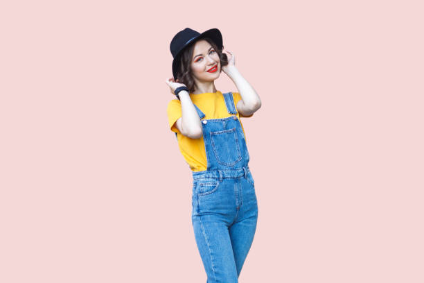 istock Charming hipster woman in blue denim overalls looking at camera with positive expression. 2001285370