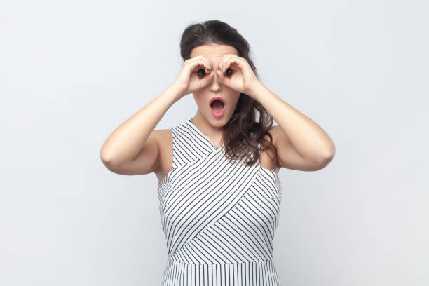 istock Surprised interested woman making binoculars gesture with hands and looking amazed at camera. 2001287428