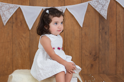 Portrait of cover girl in doll image 6-7 year old posing hands to side at black, frozen look position. Cute kid model in white dress isolated in shadow. Theatrical performance concept. Copy ad space