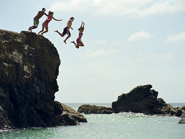 gruppo di amici di saltare nell'oceano dalla scogliera di roccia - cliffside foto e immagini stock