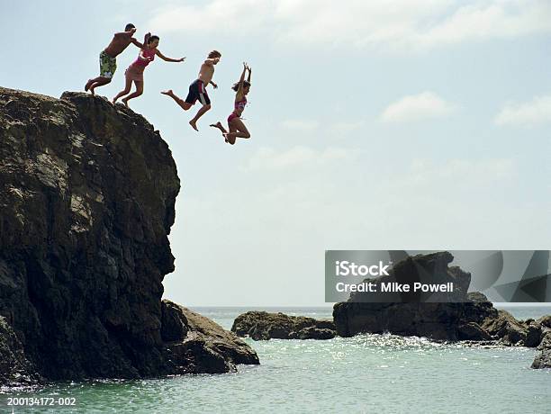 Group Of Friends Jumping Into Ocean From Rock Cliff Stock Photo - Download Image Now