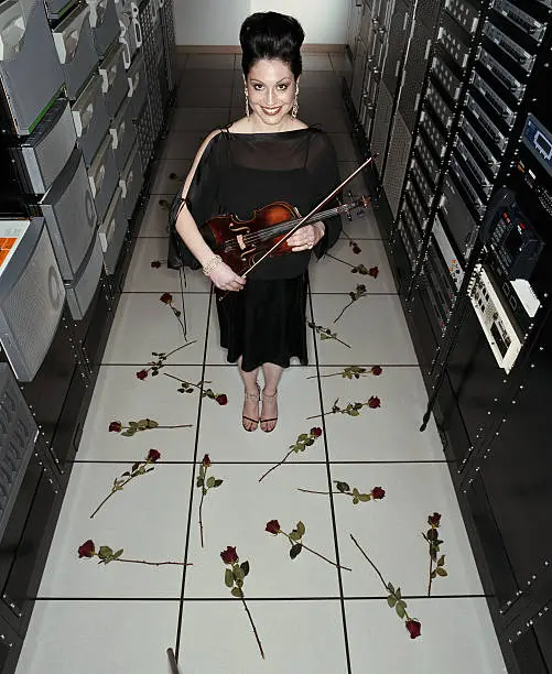 Photo of Woman holding violin, standing in server room strewn with roses