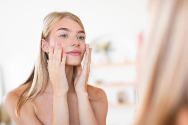 istock Pretty blonde woman applying moisturizer to face touching cheeks indoors 2001377978