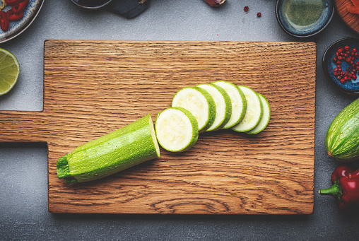 Food and cooking background. Wooden cutting board with chopped zucchini. Paprika, vegetables, spices and ingredients for cooking vegan Asian dishes with ginger, garlic, soy sauce, top view
