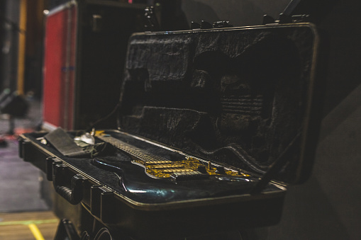 This image shows an electric guitar stored in a case backstage on an amphitheater stage before the start of the concert. The musical instrument waits silently in the wings, ready to be used during the musical event. This behind-the-scenes look offers a peek at the equipment and preparations needed to provide high-quality entertainment during the concert. The guitar, a Fender model, rests in its case alongside other audio equipment, highlighting the importance of backstage organization by roadies and the entire stage production team at musical events.