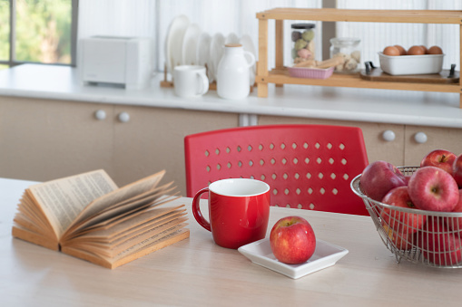 Red apple and red cup place on table in kitchen, prepare breakfast on the kitchen table, kitchen background