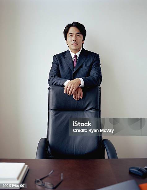 Mature Businessman Standing Behind Chair In Office Portrait Stock Photo - Download Image Now