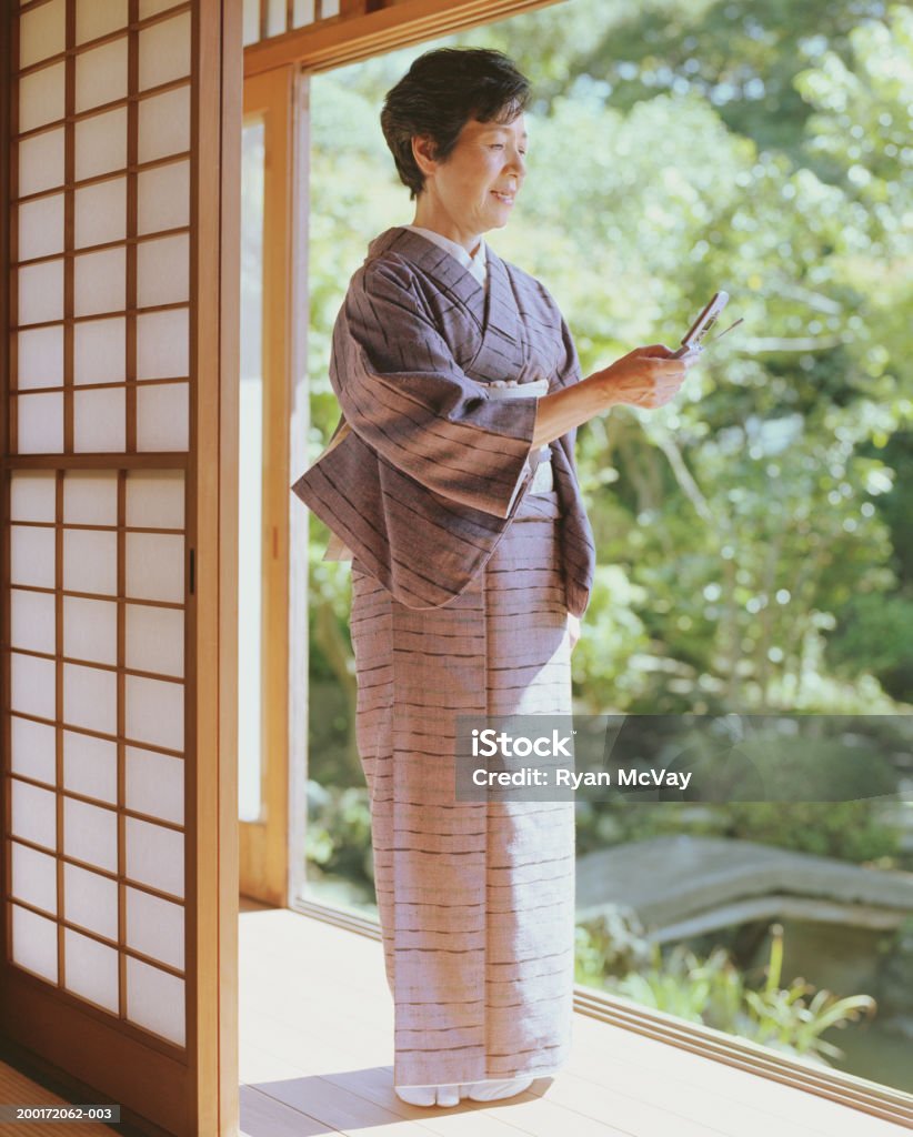 Senior femme en kimono debout dans nos portes, une ligne téléphone portable - Photo de Kimono libre de droits