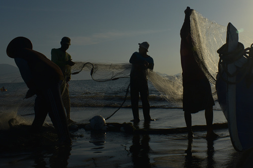 On July 23, 2017, along the shores of the Javanese village of Banda Aceh, the silhouette of fishermen meticulously cleaning traditional shore nets was a common sight. Against the backdrop of the coastal sunset, their figures moved with practiced grace, tending to the intricate mesh of the nets. The rhythmic sound of waves accompanied their task, blending with the tranquil ambiance of the village. This scene captured the timeless essence of coastal livelihoods, highlighting the enduring traditions cherished by the Acehnese fishermen.