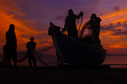 Fishermen Banda Aceh are repairing their fishing nets on the beach at sunset. In the reddish-orange glow of twilight, they diligently clean the nets from the day's catch. A peaceful atmosphere is created amidst the shimmering sea, while the sky welcomes the night with captivating warmth. Banda Aceh-Indonesia  10/20/2017