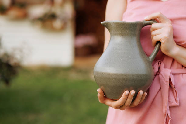 A woman in a pink dress holds a gray ceramic jug outdoors. Concept of handicraft ceramics or natural farm dairy products.
