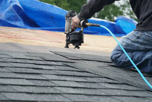 Photo of handyman using nail gun to install shingle to repair roof