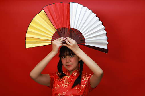 Joyful Young Asian girl with a traditional cheongsam dress call qipao several action with multicolor hand fan on Chinese New Year's Day