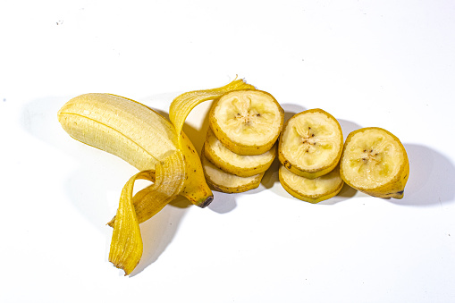 several pieces of banana cut into small pieces and one whole banana served on a plain white base