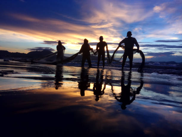 Fishermen Banda Aceh are repairing their fishing nets on the beach at sunset. In the reddish-orange glow of twilight, they diligently clean the nets from the day's catch. A peaceful atmosphere is created amidst the shimmering sea, while the sky welcomes the night with captivating warmth. Banda Aceh-Indonesia. 10/21/2018