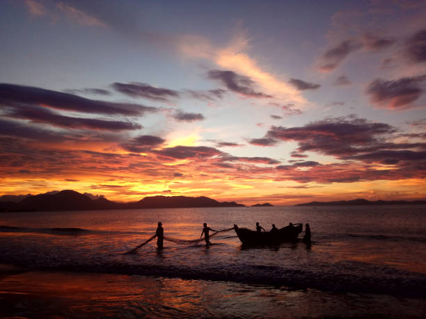 Fishermen Banda Aceh are repairing their fishing nets on the beach at sunset. In the reddish-orange glow of twilight, they diligently clean the nets from the day's catch. A peaceful atmosphere is created amidst the shimmering sea, while the sky welcomes the night with captivating warmth. Banda Aceh-Indonesia. 10/21/2018