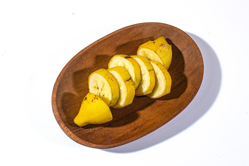 Bananas are cut into several pieces and served on a wooden plate with a plain white background