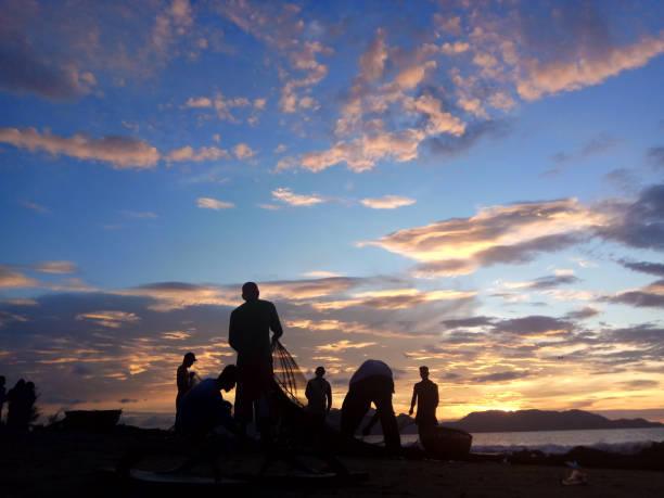Fishermen Banda Aceh are repairing their fishing nets on the beach at sunset. In the reddish-orange glow of twilight, they diligently clean the nets from the day's catch. A peaceful atmosphere is created amidst the shimmering sea, while the sky welcomes the night with captivating warmth. Banda Aceh-Indonesia 04/03/2019